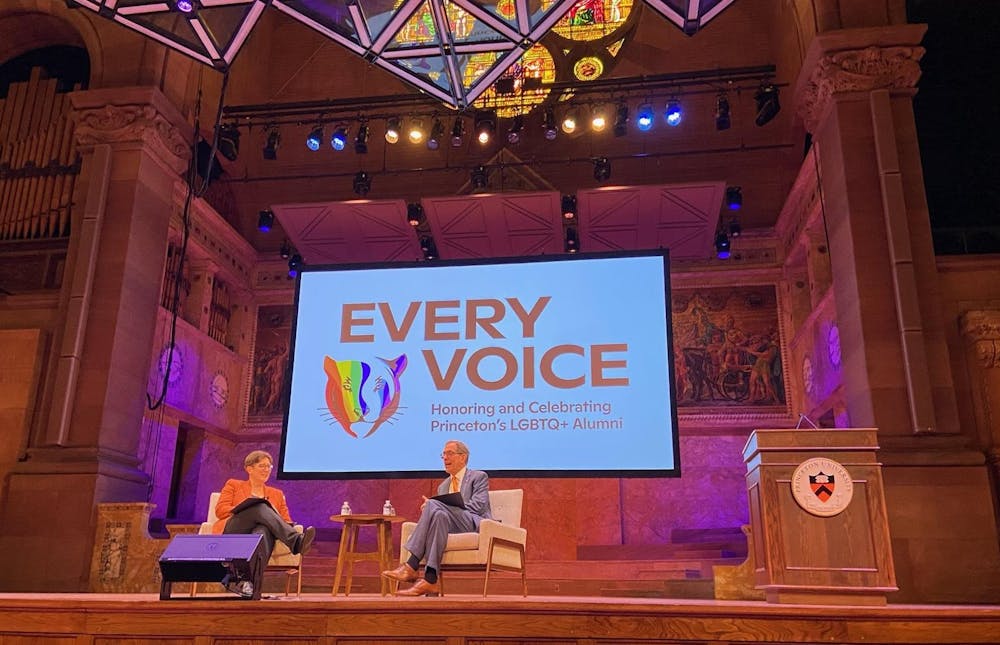 Two people sit in chairs on a stage, in front of a screen that reads, "Every Voice: Honoring and Celebrating Princeton's LGBTQ+ Alumni"