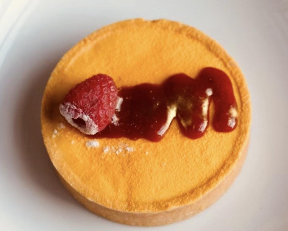 A yellow pastry with red sauce and a raspberry on top.