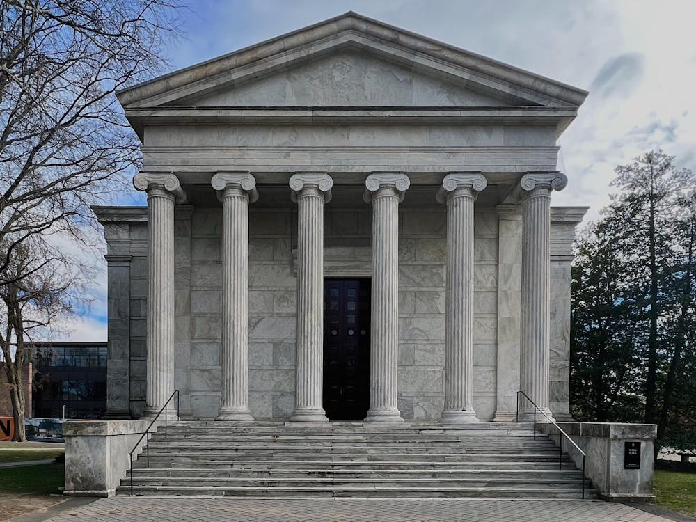 A white, marble building with columns and a brown door.