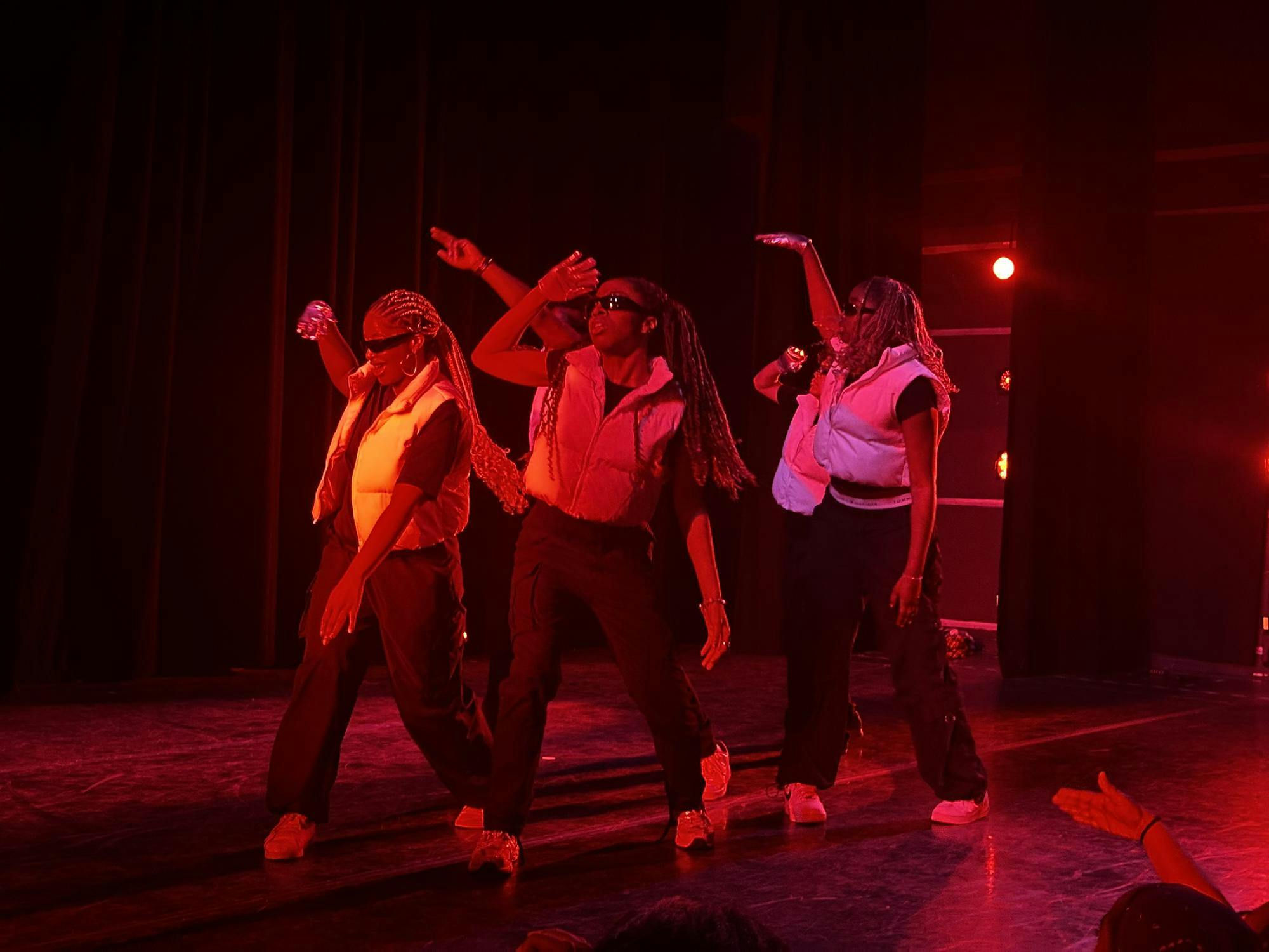 Four dances pose on stage in a white vest in black sunglasses.