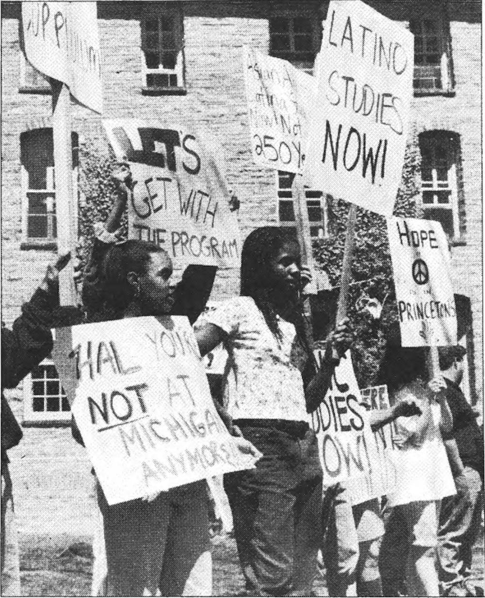 Students protest outside Nassau Hall holding signs.