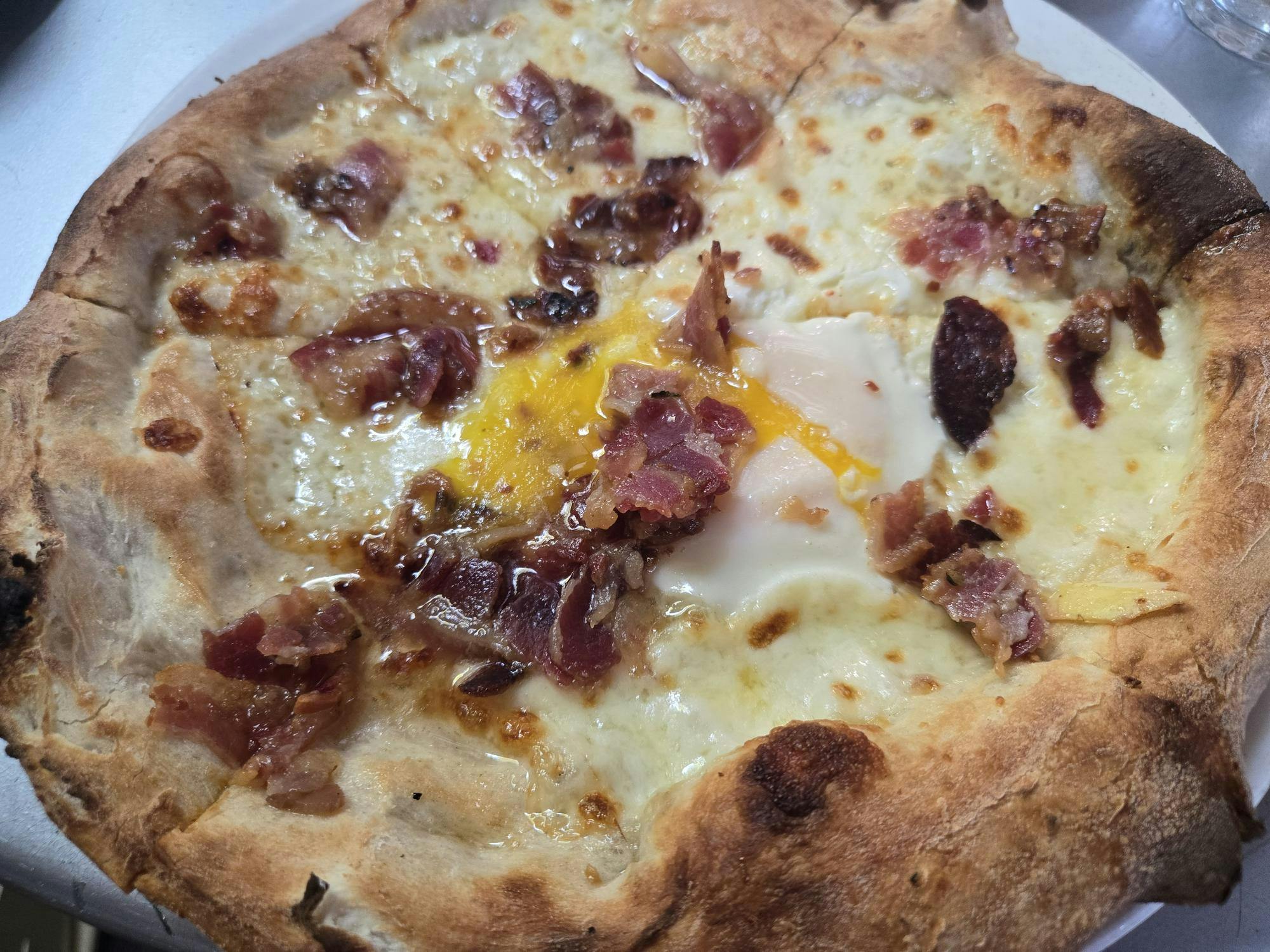 A close up of a breakfast pizza consisting of pancetta, fior di latte, egg, and rosemary.