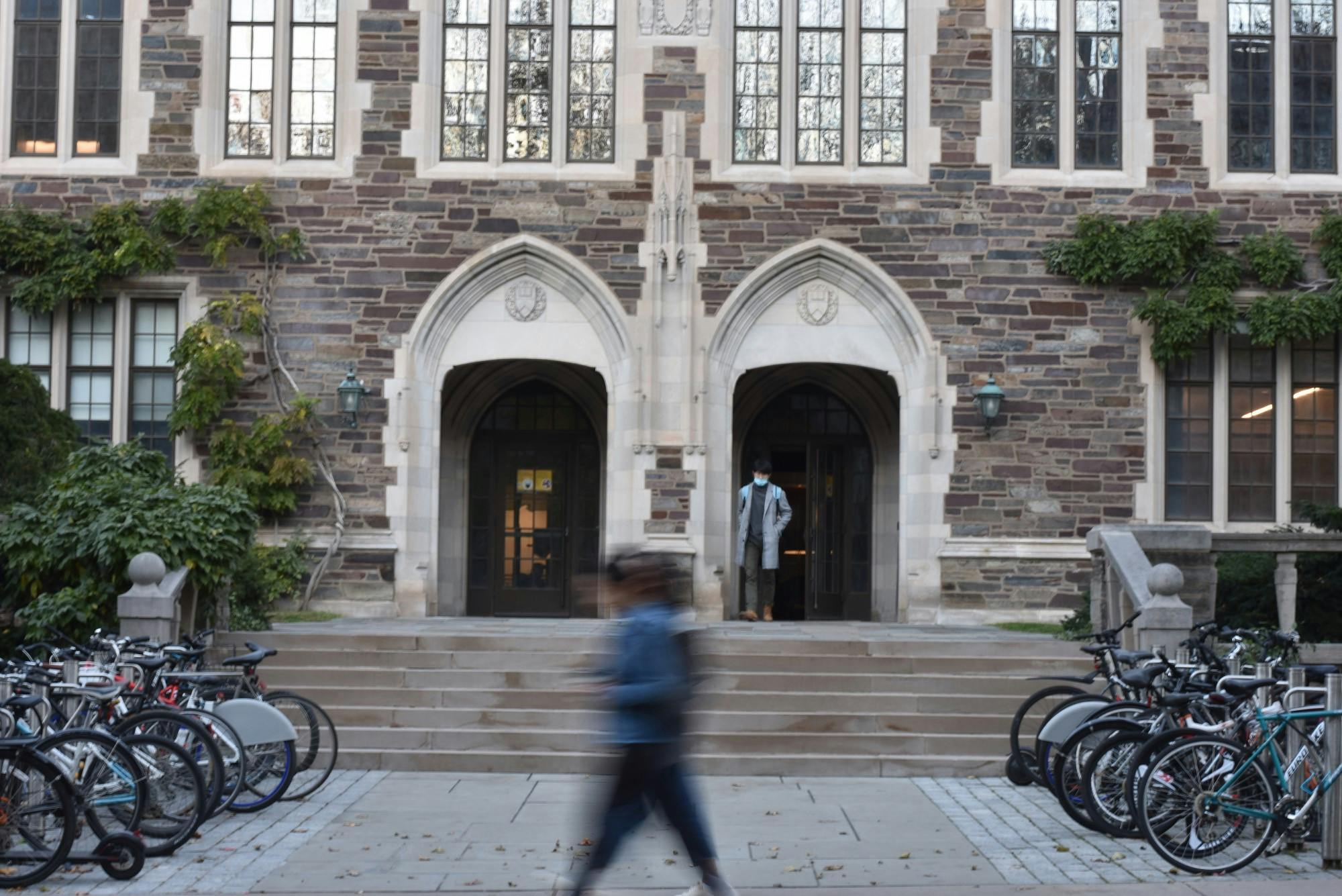 A blurry person walks in front of the double arched entry to a building. 