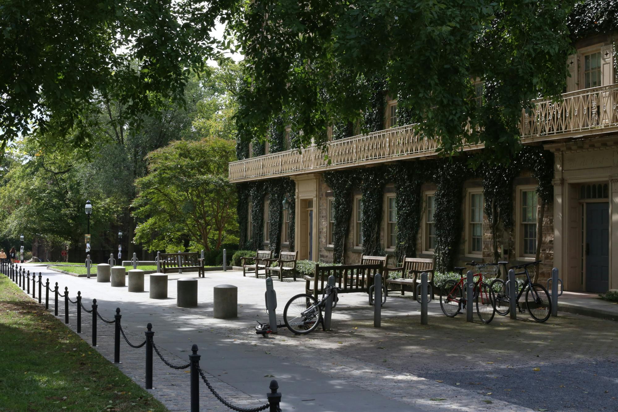 An ivy-covered building with brightly lit benches and a bike rack in front.