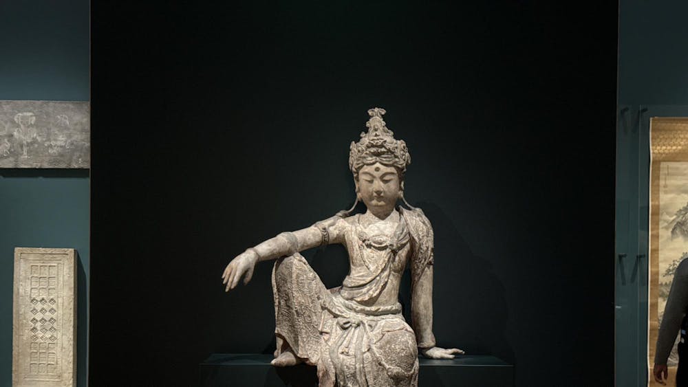 A grey stone statue sits behind a black background in a large room.