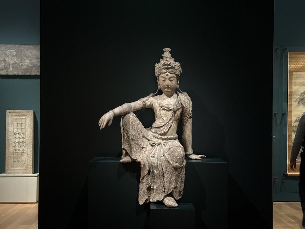A grey stone statue sits behind a black background in a large room.
