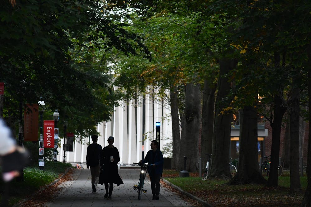 Three people are walking down a path with trees and a building behind them. 