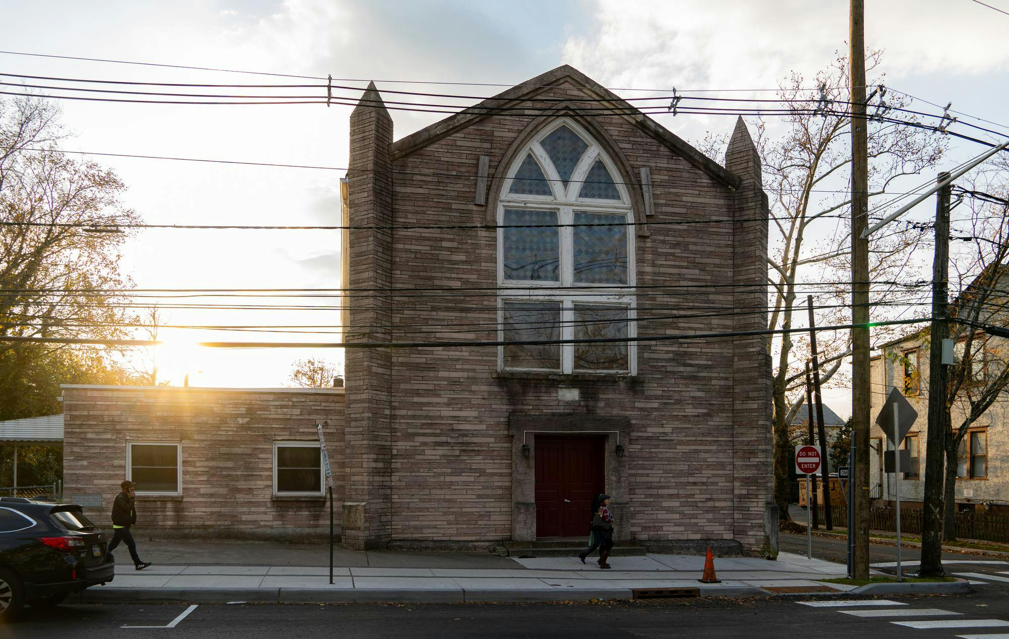 A large stone building with a large window in the center of the building is featured. The building has a red door, which a person is walking in front of.