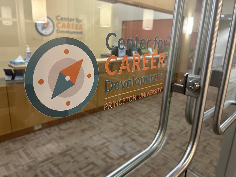 A glass door with a sticker showing a compass and orange and blue text. A desk with a box of tissues and hand sanitizer are visible. 