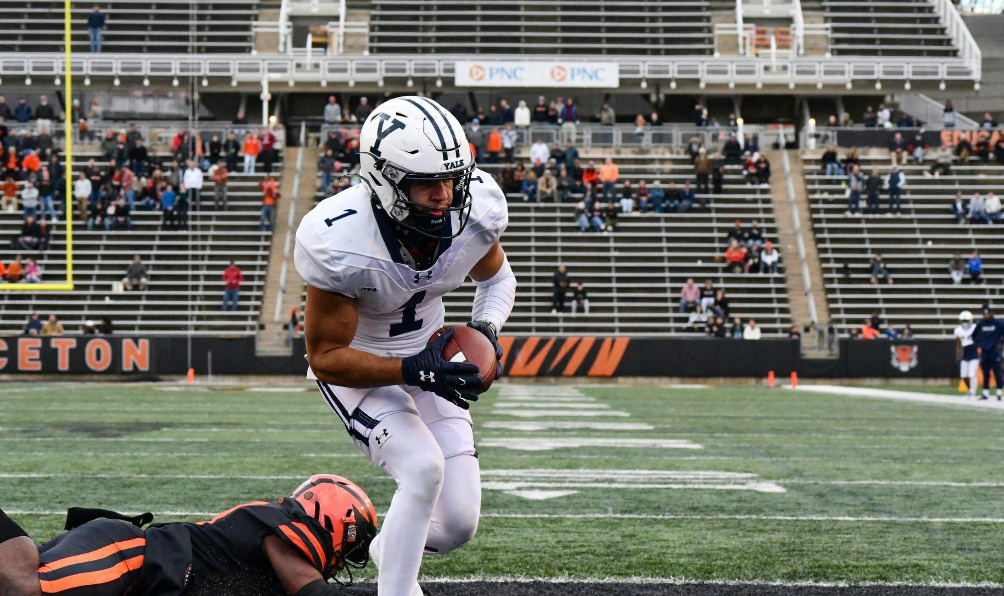 A Yale football player succesfully catching the football in the end zone while a Princeton player unsuccesfully attempts to tackle him.