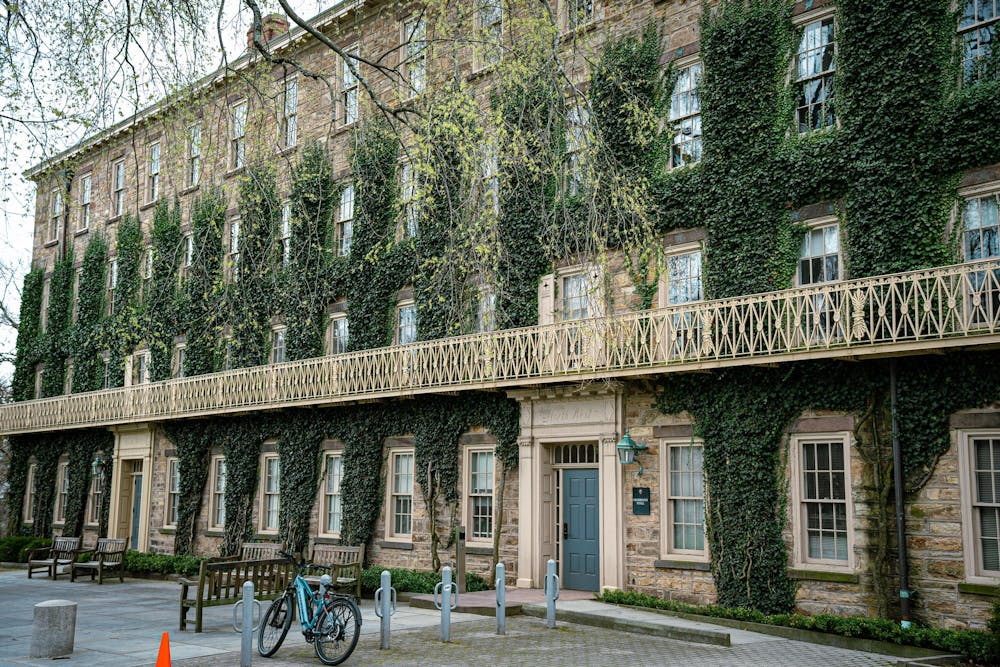 A large, ivy-covered building looms in front of the camera. Benches and bike racks are outside. 