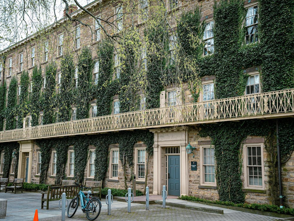 A large, ivy-covered building looms in front of the camera. Benches and bike racks are outside.