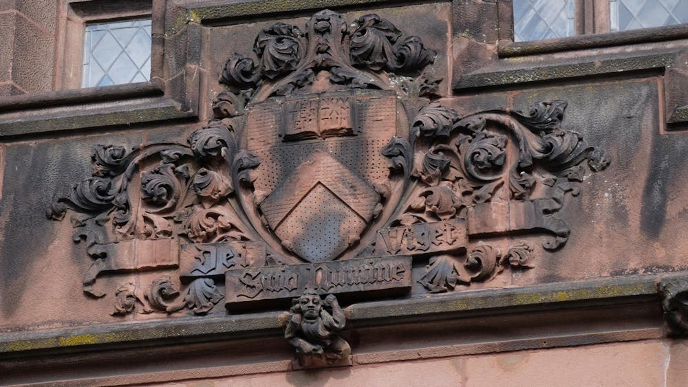 Princeton University’s coat of arms carved into an old building which is fading brown and black.