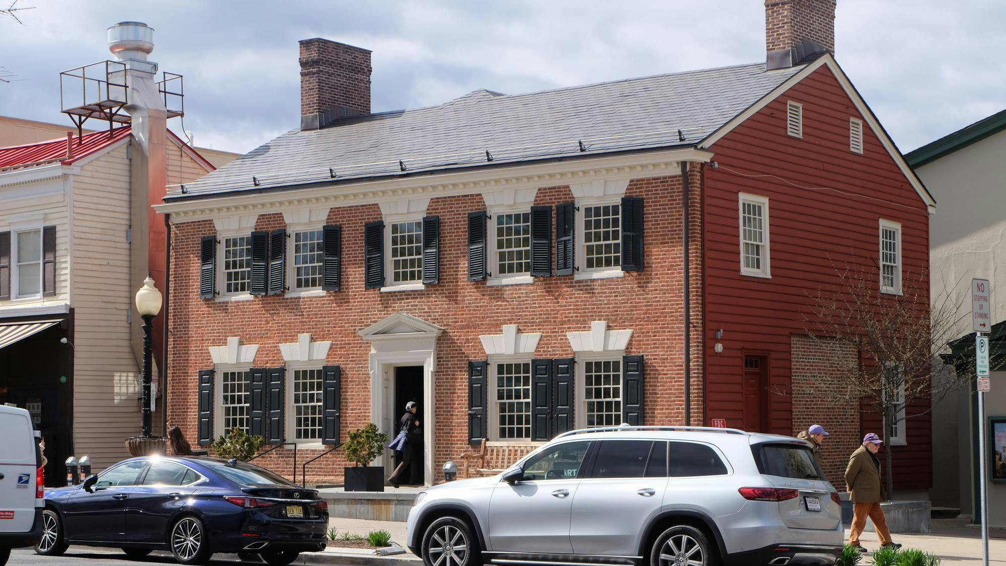A red brick building with cars parked in front, and a few people walking by.