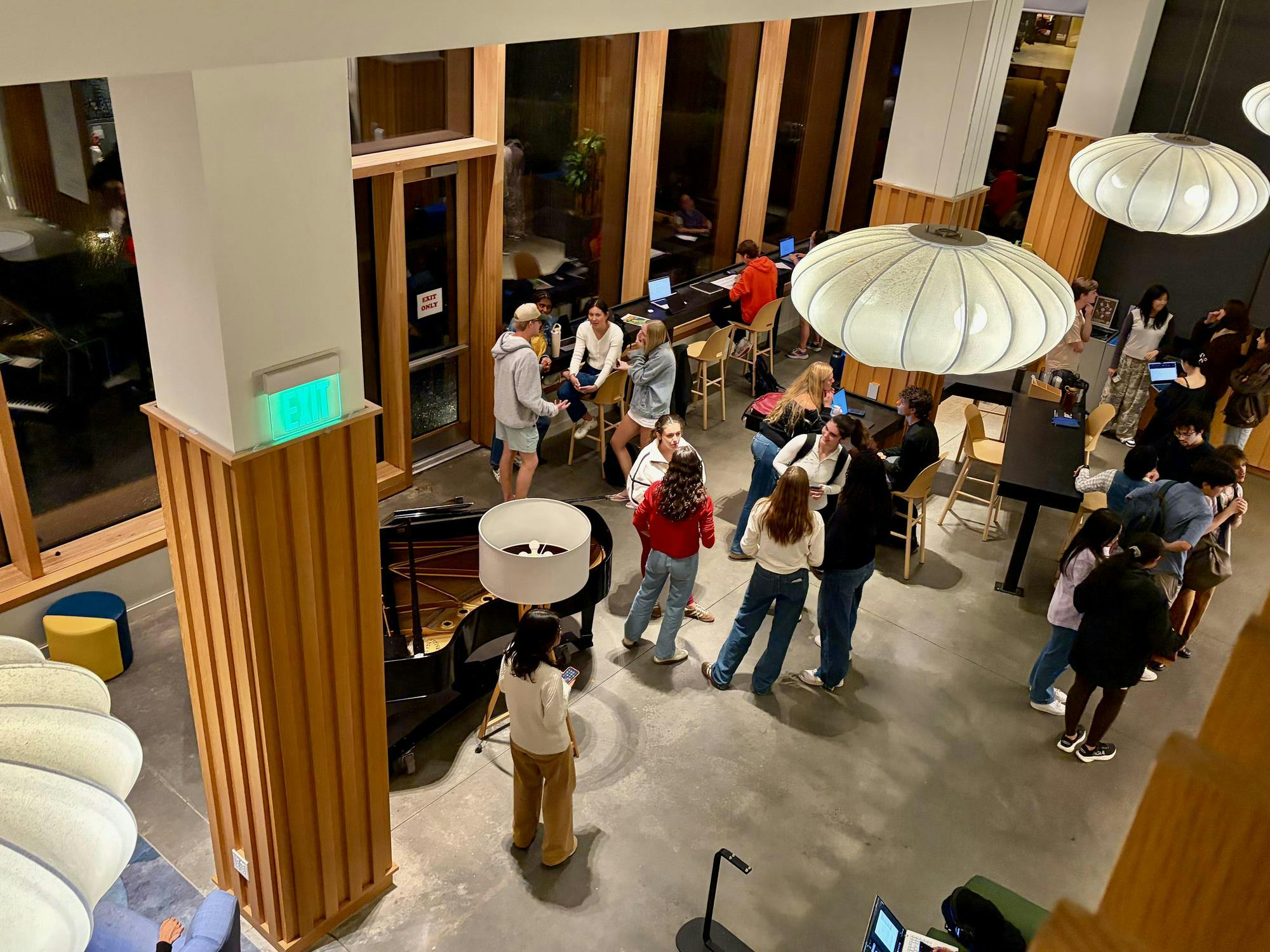 A large group of students hang out in a large open space, with bright white lights hanging overhead. 