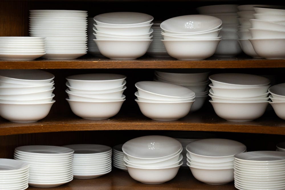 White ceramic bowls are stacked in rows on a brown wooden shelf.