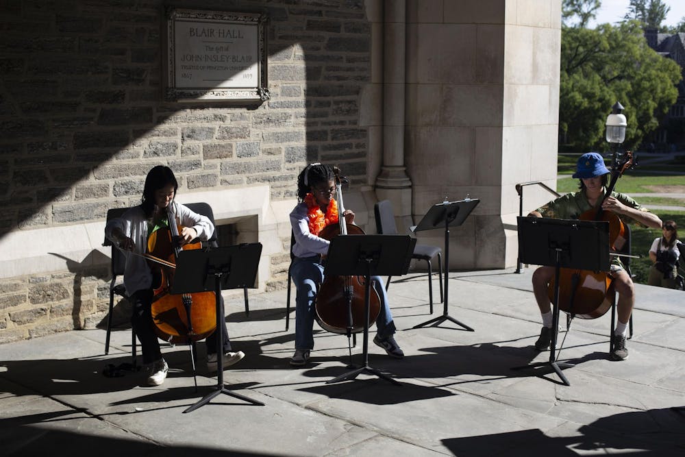 Three students sit in Blair Arch, all in chairs, playing cellos, with music stands in front of them. 