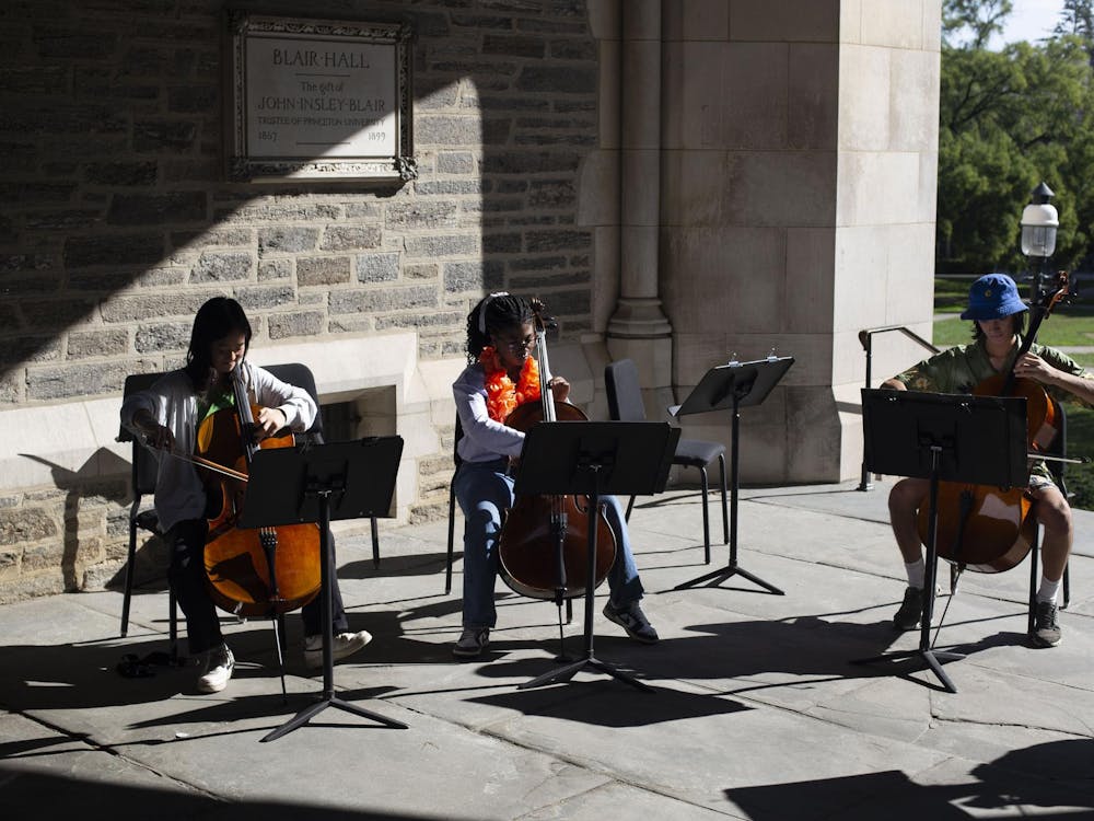 Three students sit in Blair Arch, all in chairs, playing cellos, with music stands in front of them.