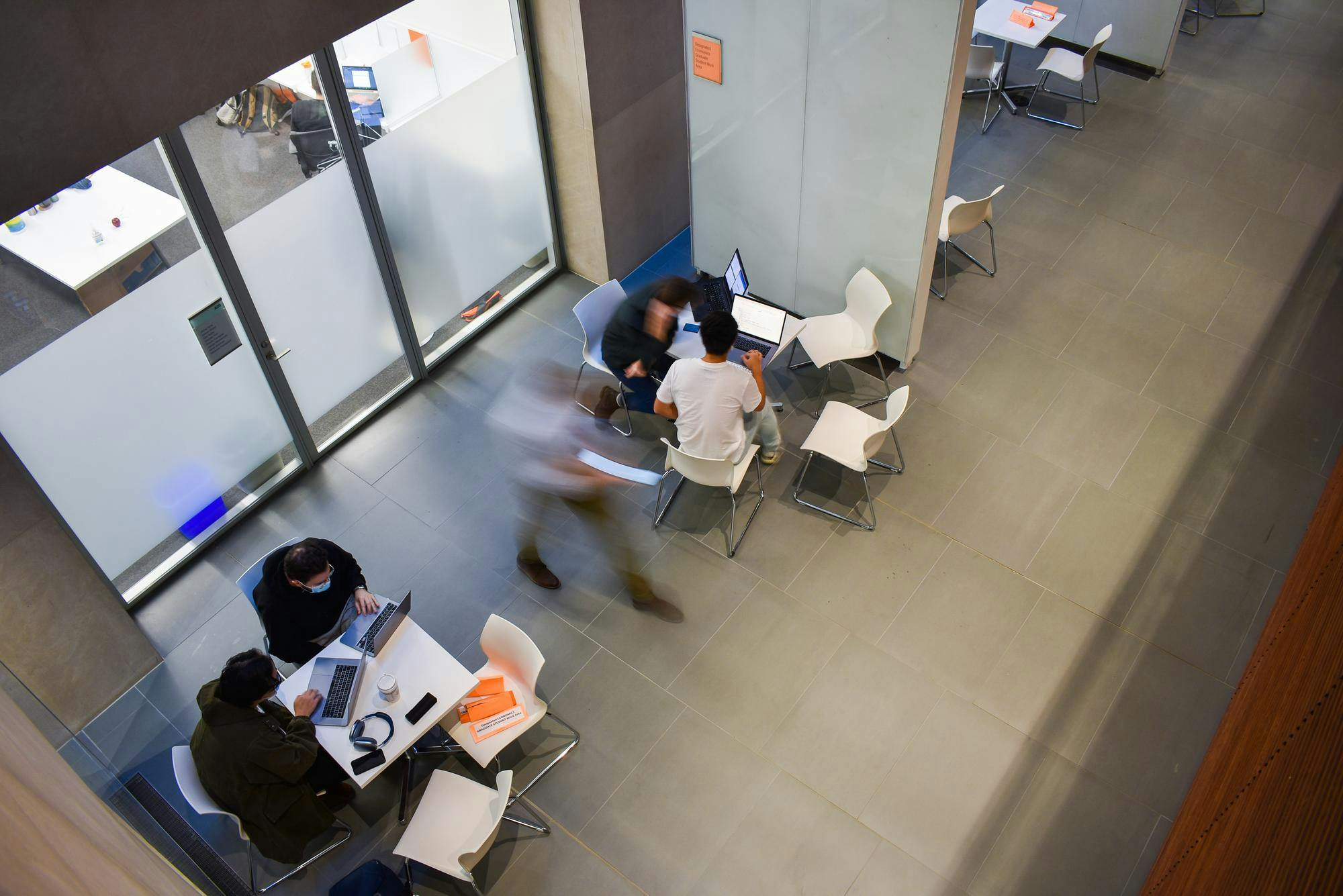 Long exposure photo of a bird's eye view of students studying at tables and by whiteboards.
