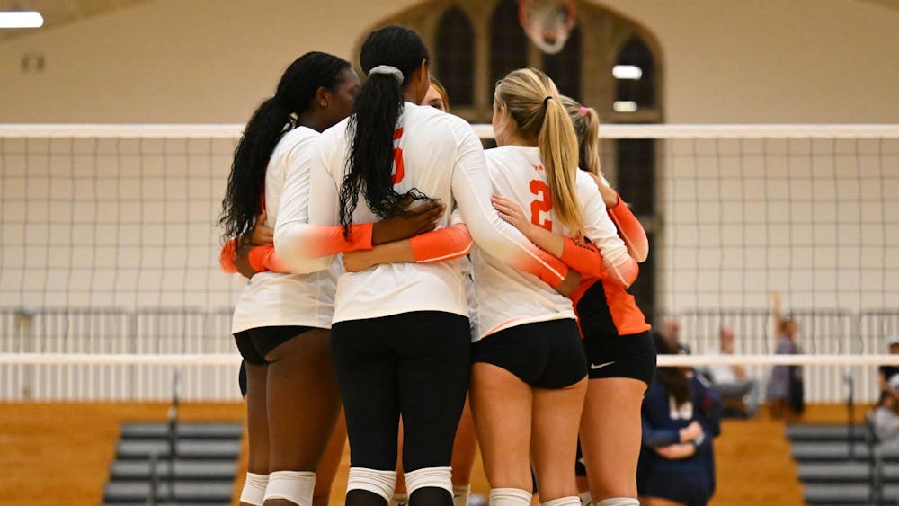 A group of volleyball players huddle in front of a net between points. 