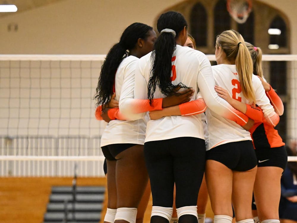 A group of volleyball players huddle in front of a net between points.