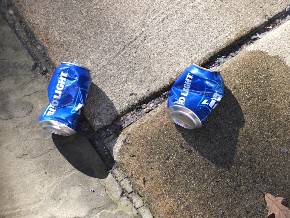 Two blue beer cans that say Bud Light sit on the wet sidewalk. 