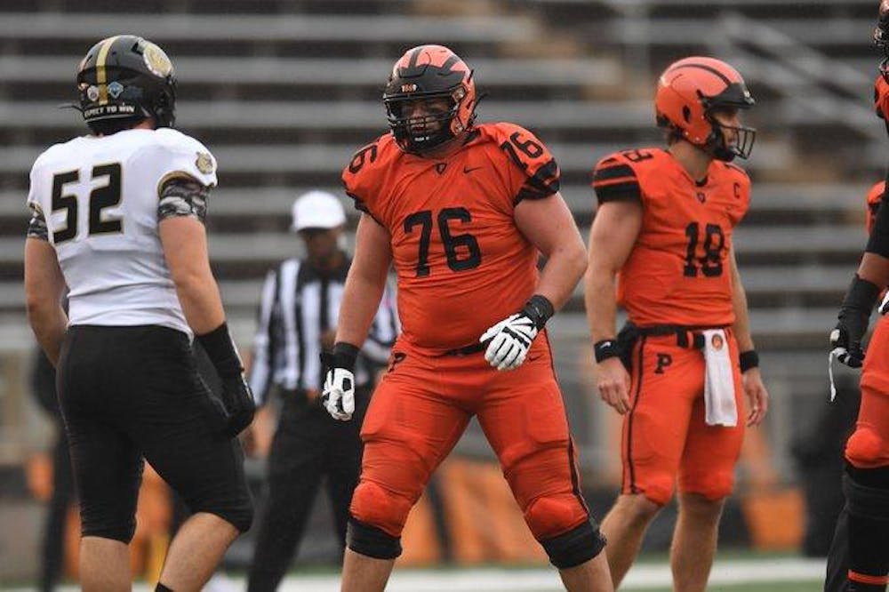 An offensive lineman in an orange and black uniform stands on field as offense looks to start play.