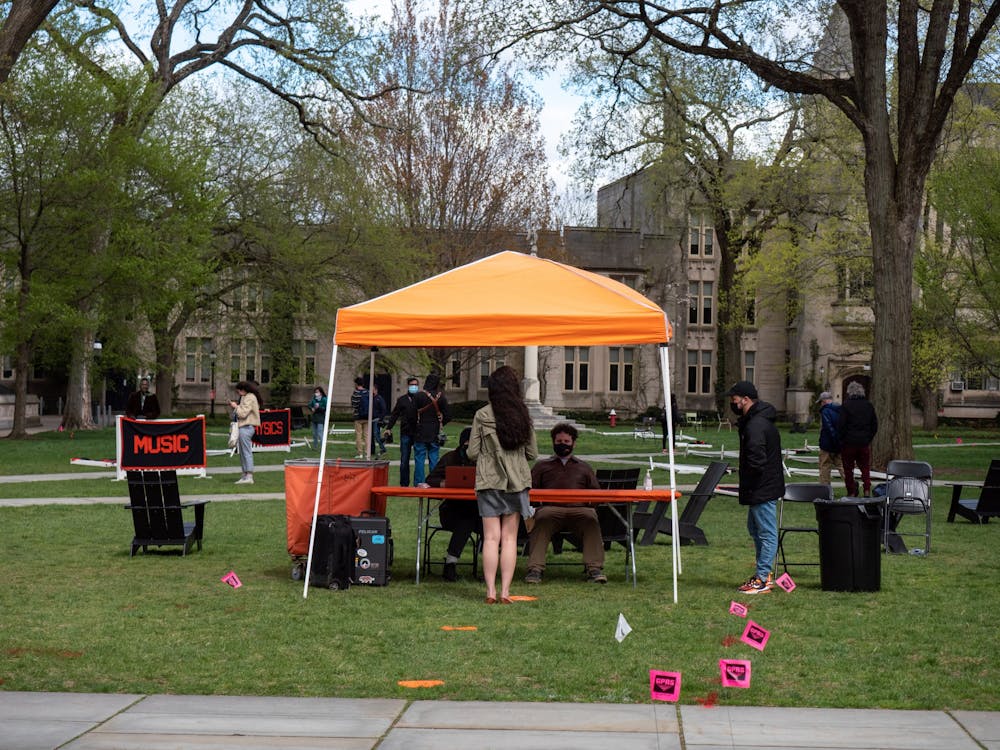 A student faces two people sitting at a table underneath an orange tent. On the lawn, there are concentration banners including Music and Physics.