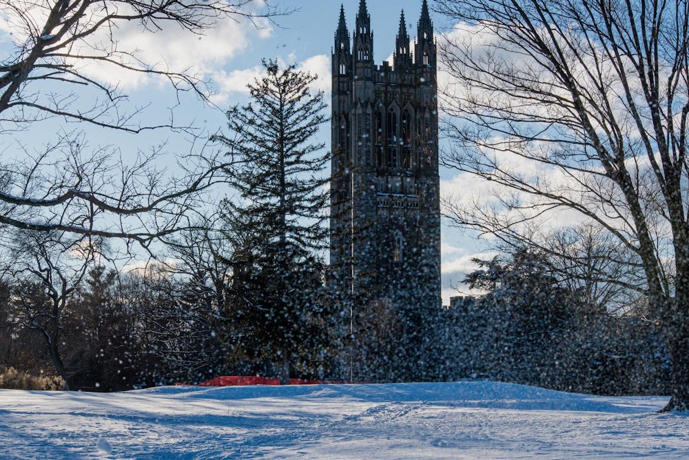 Snow falls across Princeton University’s campus as the Graduate College tower rises behind trees on a winter afternoon.