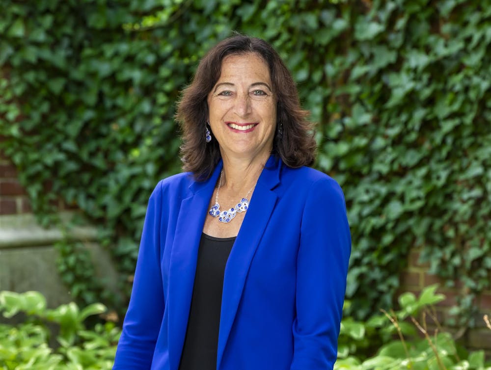 A woman wearing a blue vest with a black top taking a picture in front of a green background 