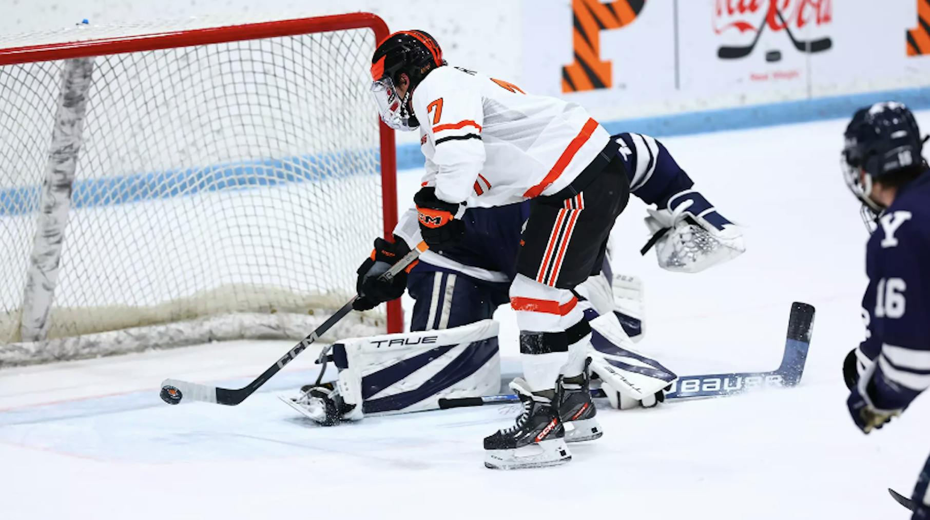 Hockey player hits puck right in front of goal while goalie lies on ice
