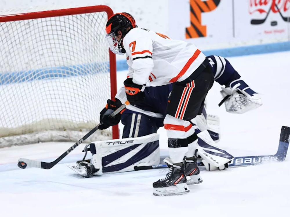Hockey player hits puck right in front of goal while goalie lies on ice