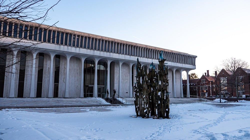 A large building with white columns stands behind a gray structure. The ground is covered in snow.
