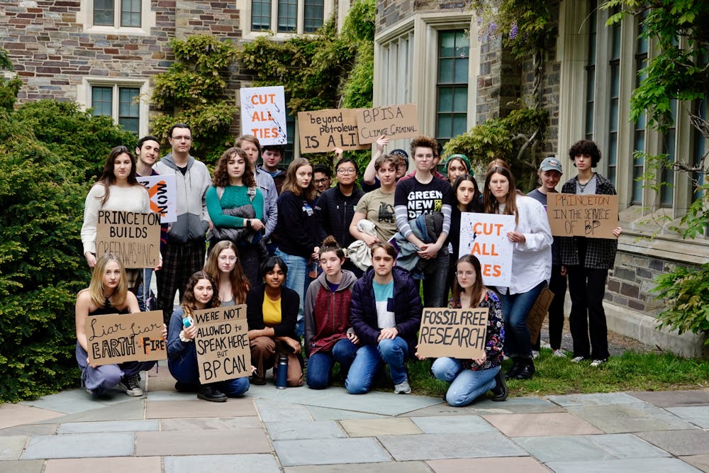 A group of students are gathered in a green courtyard, standing and kneeling with cardboard signs held up.