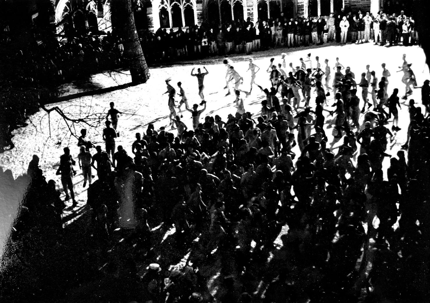 Several naked participants run across the snow in Holder courtyard. The photo is black and white and is taken out of a window overlooking the courtyard.