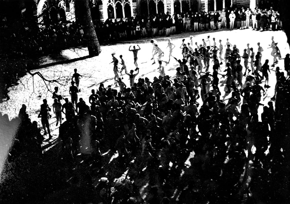 Several naked participants run across the snow in Holder courtyard. The photo is black and white and is taken out of a window overlooking the courtyard.