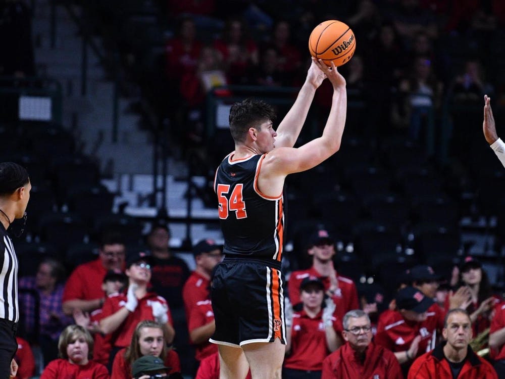 A basketball player in a black and orange jersey shoots a basketball in front of a sea of red-wearing Rutgers fans.
