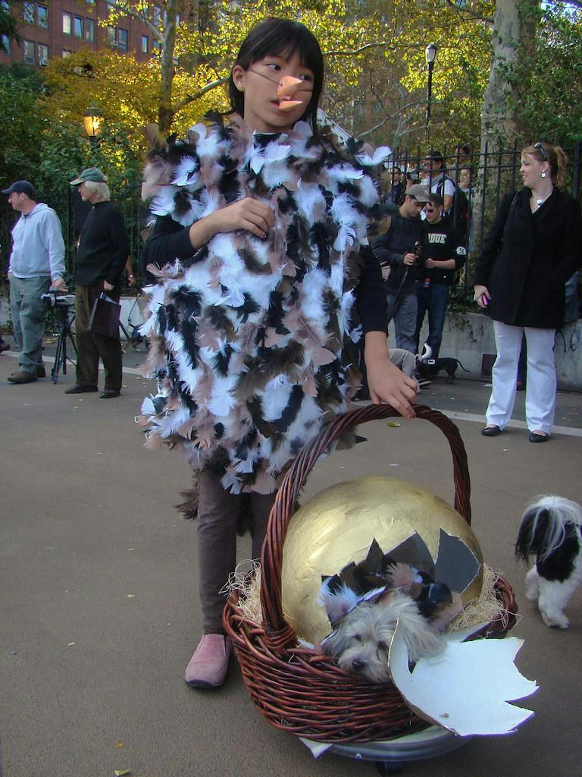 A girl dresses as a feathery bird and holds a basket that contains an egg.