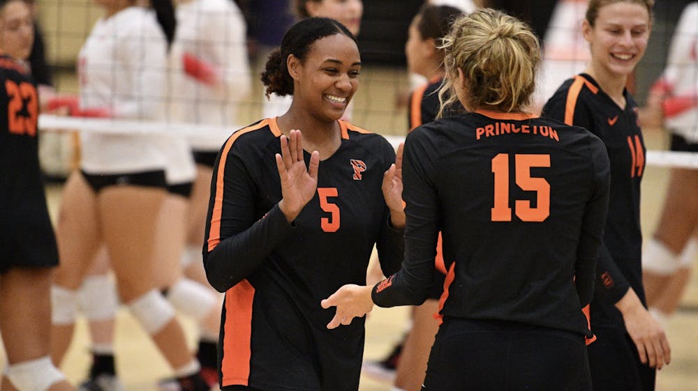 Two women's volleyball players high five with both hands on court