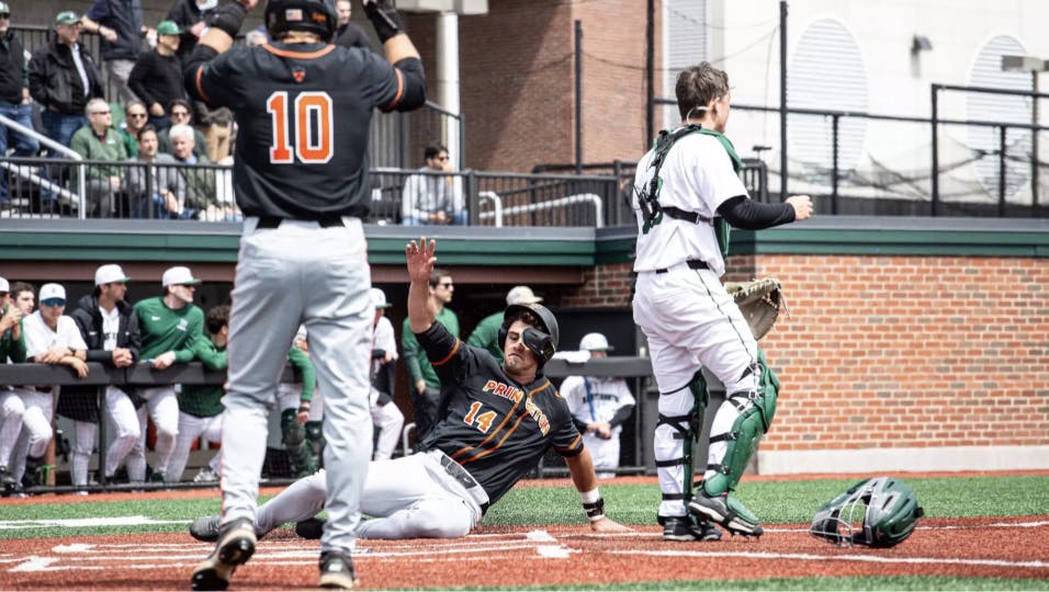A baseball player in a black jersey sliding into home plate.