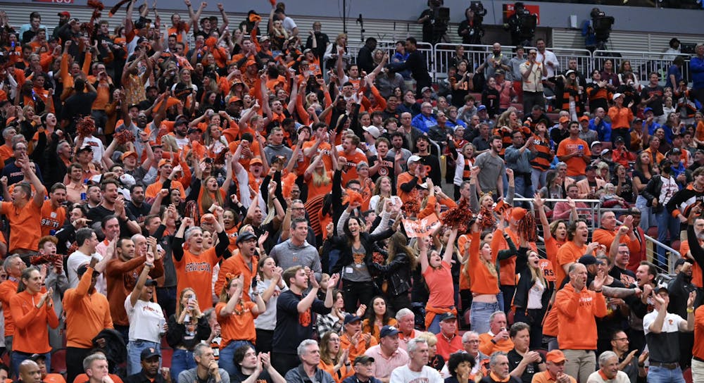 Packed bleachers of orange and black shirted fans cheering at a sporting event. 