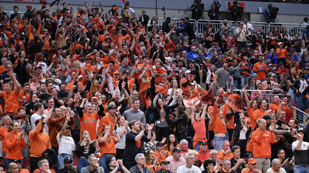 Packed bleachers of orange and black shirted fans cheering at a sporting event. 