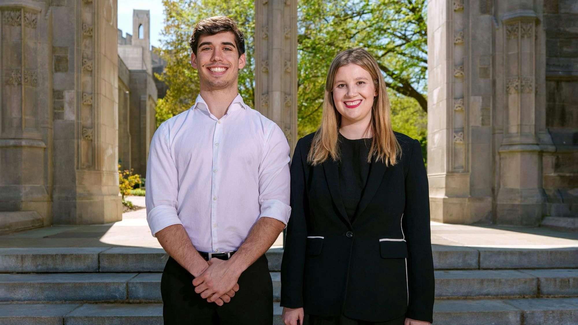 A man with brown hair and a white shirt stands next to a blonde woman in a black outfit. Behind them is gothic scenery.