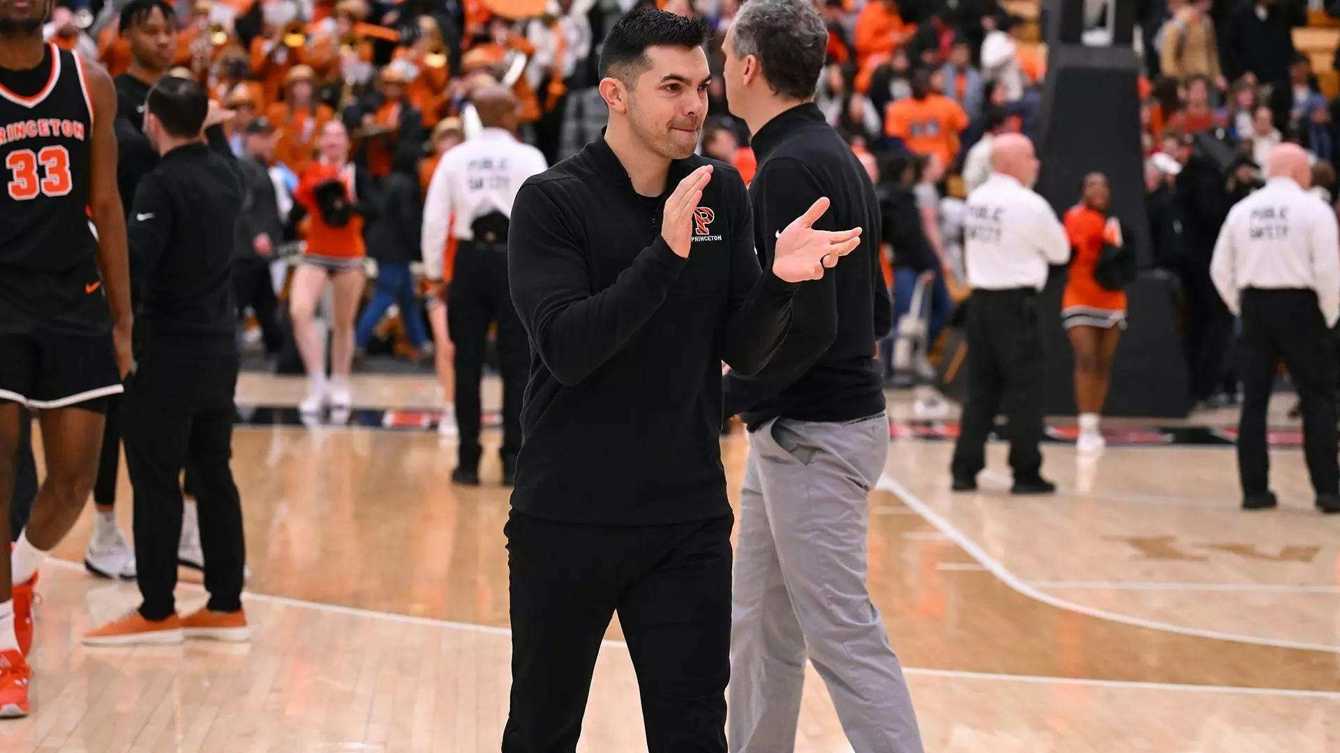 A coach wearing a Princeton quarter zip clapping on a basketball court after the end of a game.