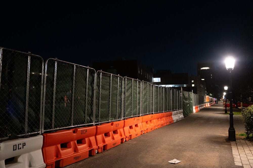 An orange barrier with a fence closes off a dark construction site.