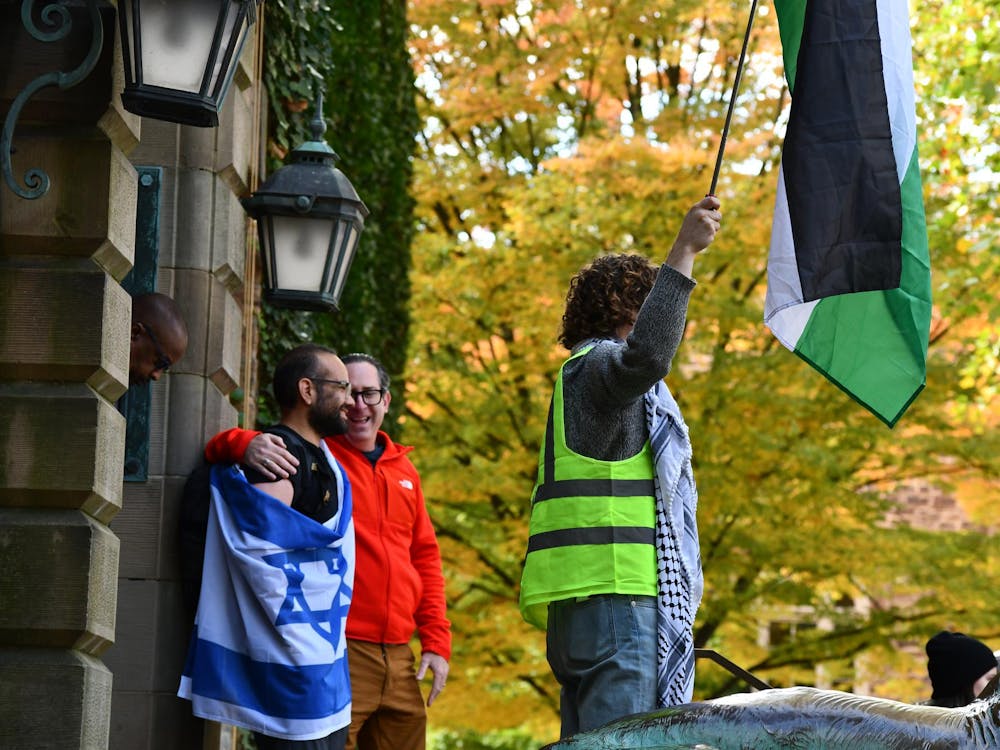 Standing behind a protestor wearing a green work vest, a keffiyeh, and holding a Palestinian flag, a man wraps himself in an Israeli flag on the steps in front of Nassau Hall. 