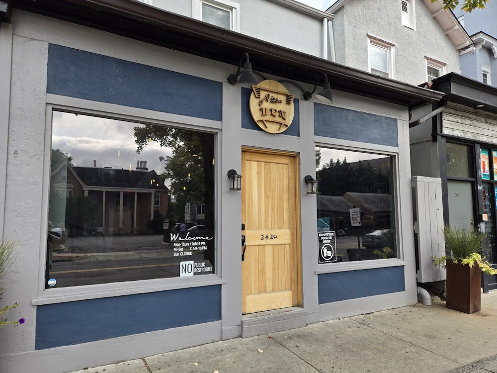 A gray and blue storefront. The wooden sign above the door says Pizza Den.