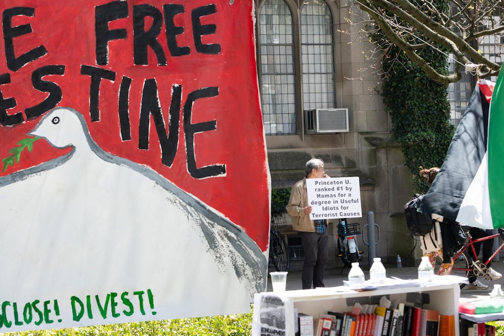 In the foreground, a banner saying "divest." In the background, a man holding a sign reading "Princeton U. ranked #1 by Hamas for a degree in Useful Idiots for Terrorist Causes."