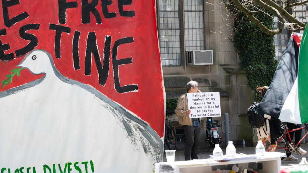 In the foreground, a banner saying "divest." In the background, a man holding a sign reading "Princeton U. ranked #1 by Hamas for a degree in Useful Idiots for Terrorist Causes."