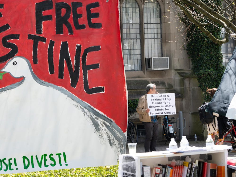 In the foreground, a banner saying "divest." In the background, a man holding a sign reading "Princeton U. ranked #1 by Hamas for a degree in Useful Idiots for Terrorist Causes."